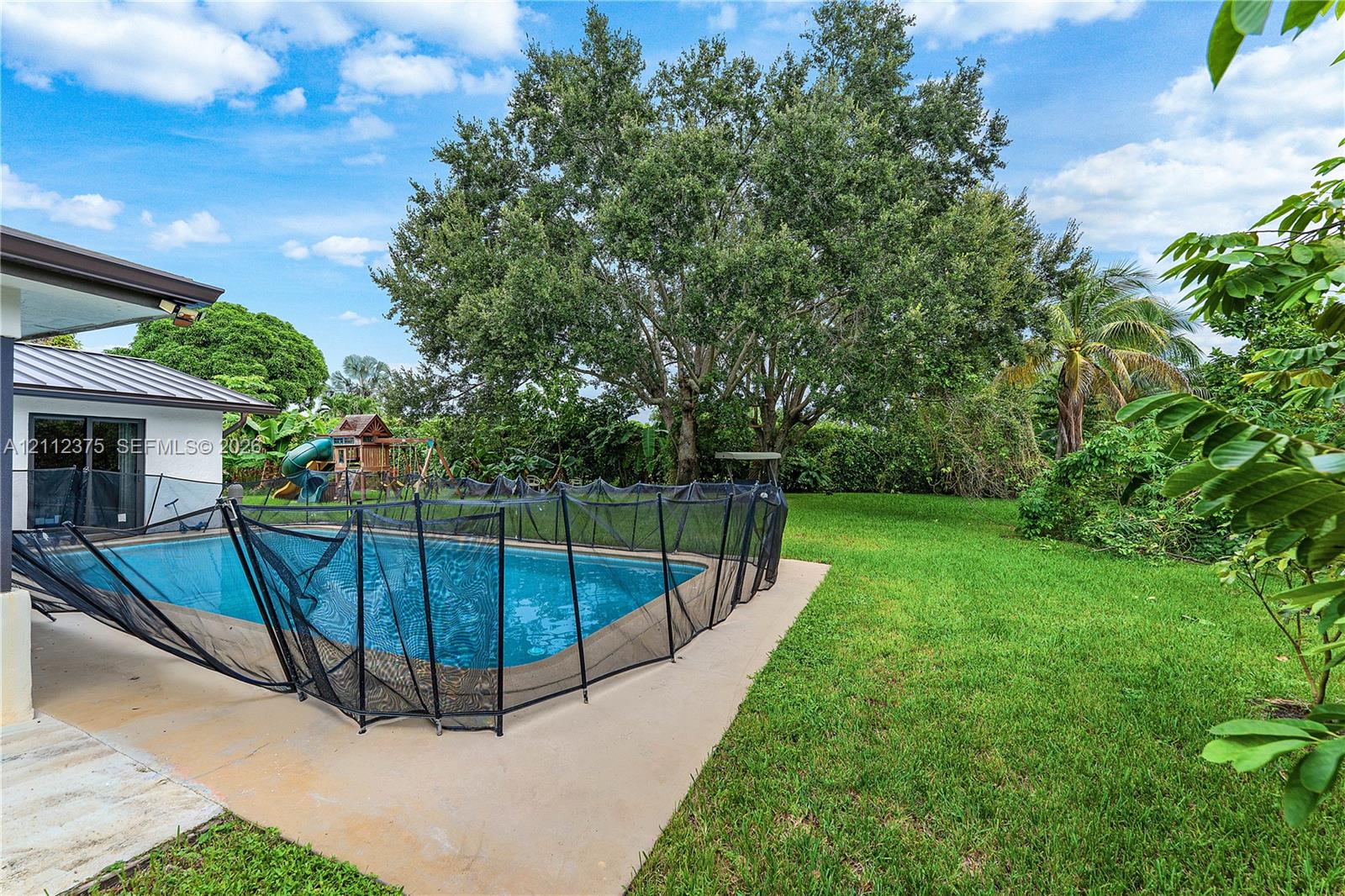 Rear exterior featuring a swimming pool, concrete patio, mature trees, and expansive lawn