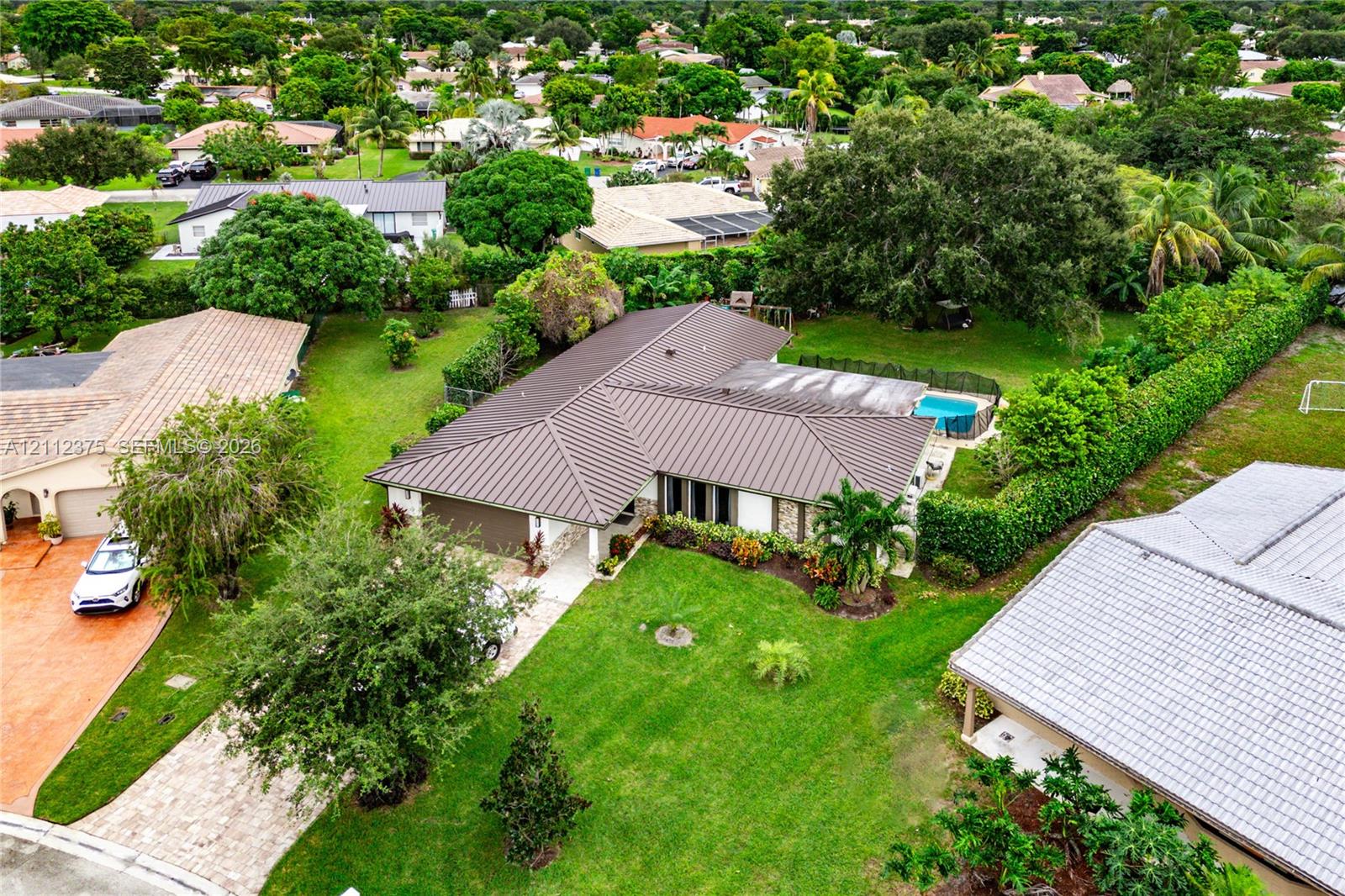 Aerial view featuring a metal roof, expansive grass lawn, mature landscaping, and a fenced swimming pool