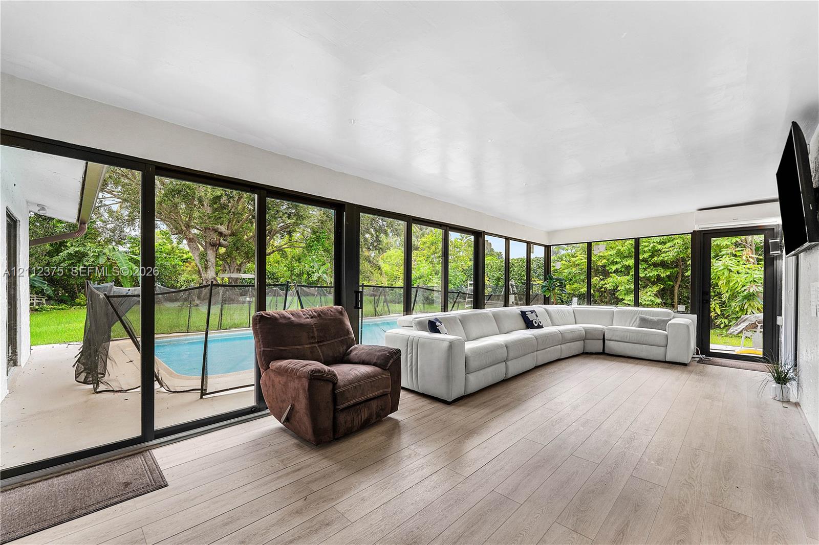 Sunroom featuring expansive floor-to-ceiling glass panel walls, wood-finish flooring, and direct access to an exterior swimming pool area