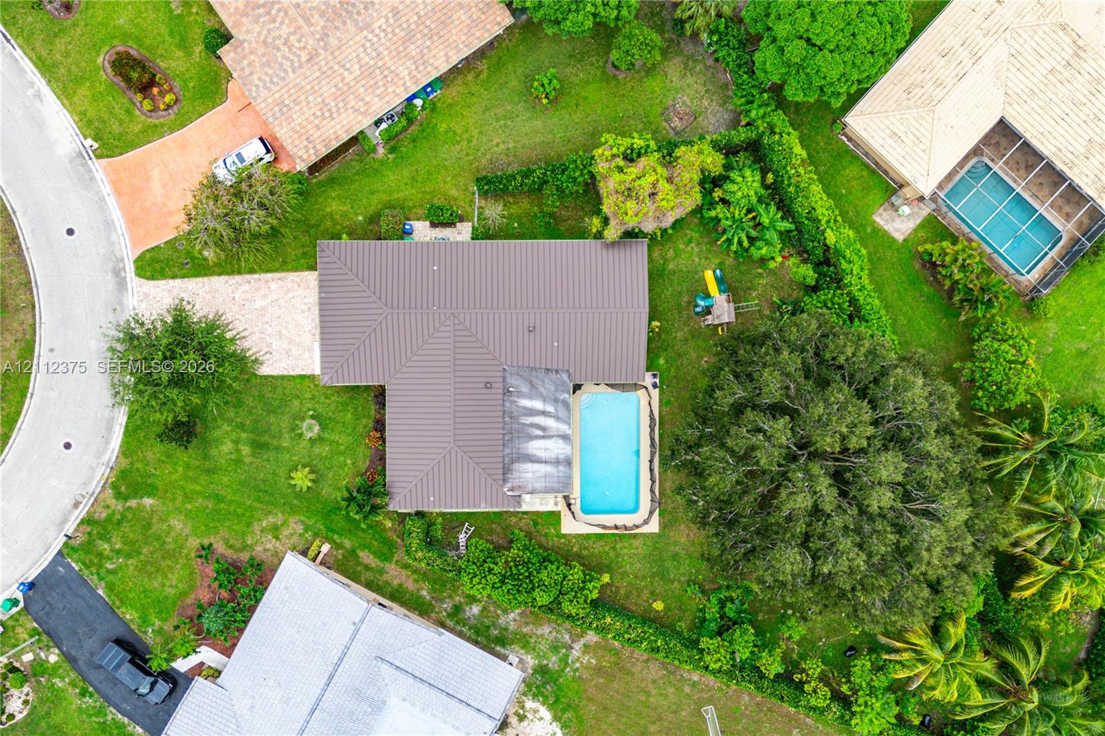 Aerial perspective featuring a metal roof, in-ground swimming pool, brick-paver driveway, and mature landscaping