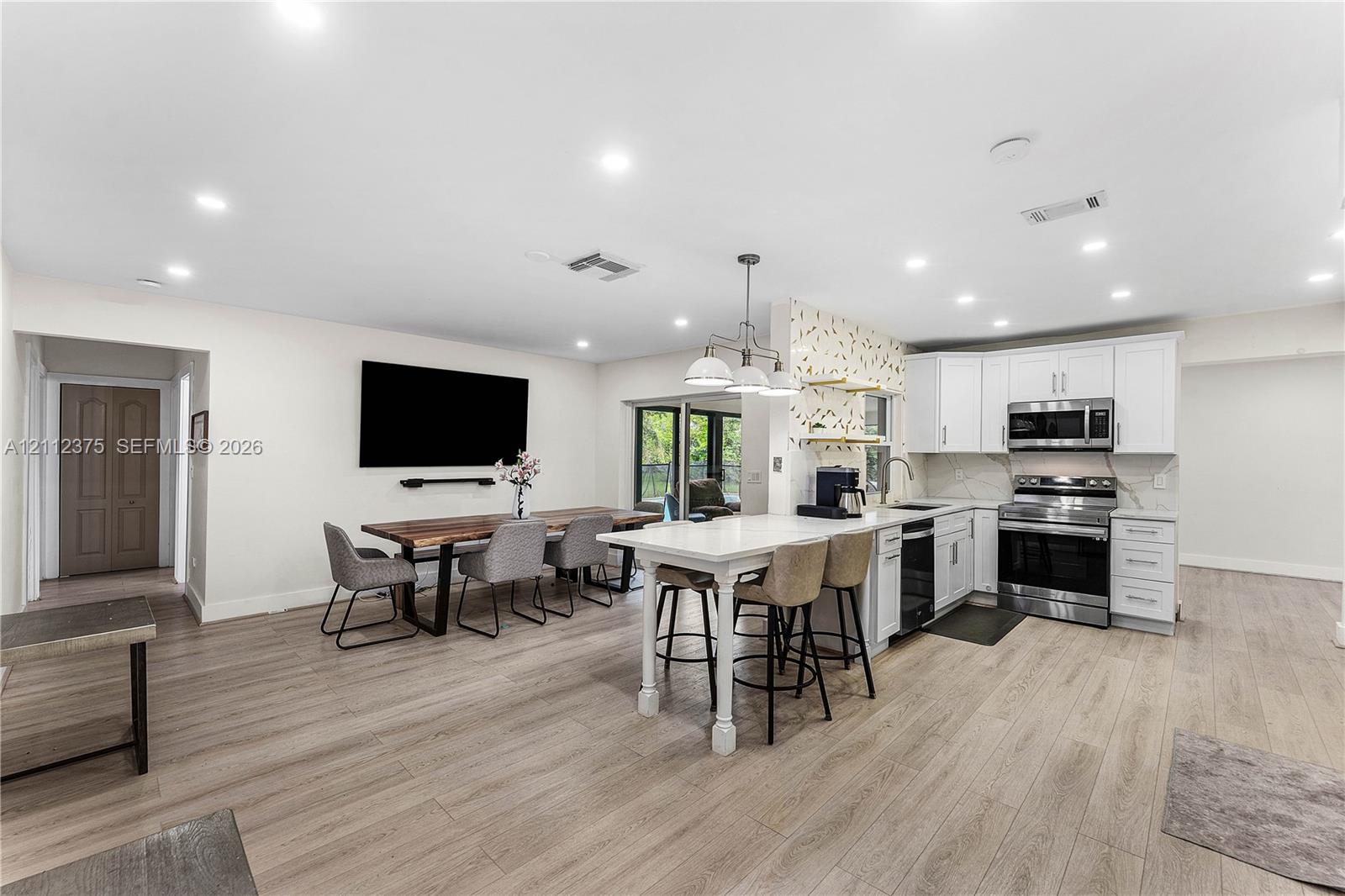 Kitchen featuring white cabinetry, stainless steel appliances, a central island with counter seating, recessed lighting, and wood-finish flooring