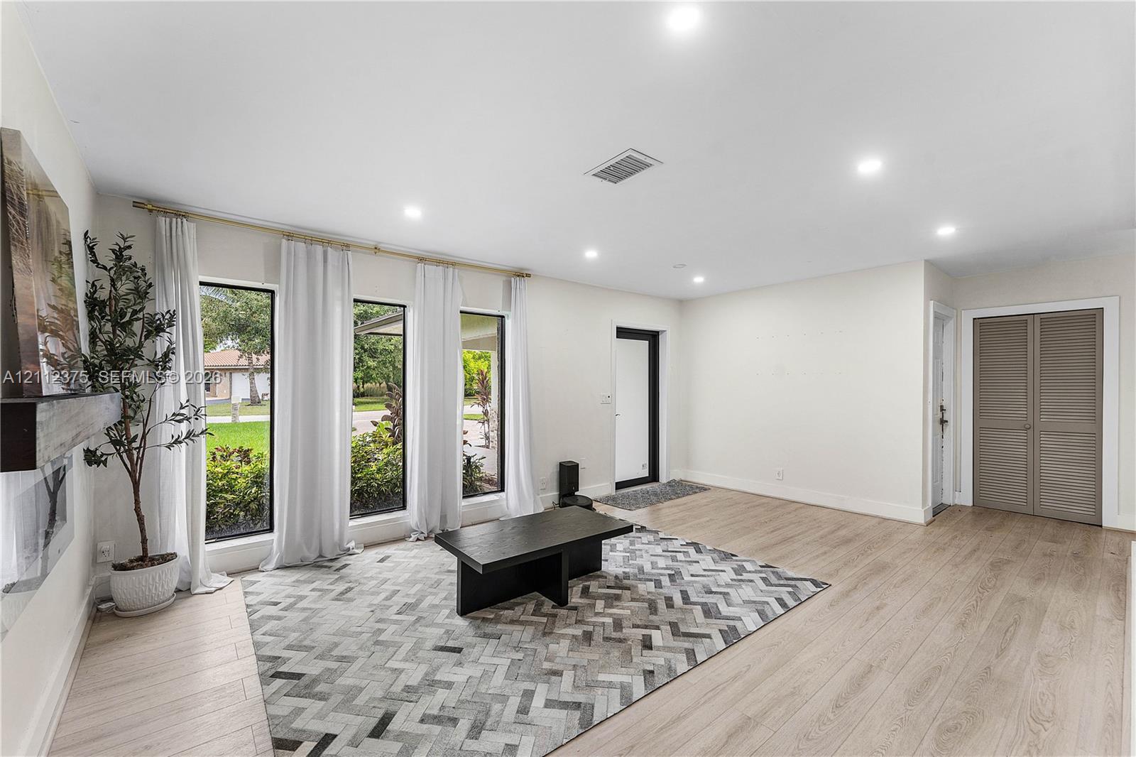 Living area featuring wood-finish flooring, recessed lighting, triple floor-to-ceiling windows, and dual-panel closet doors