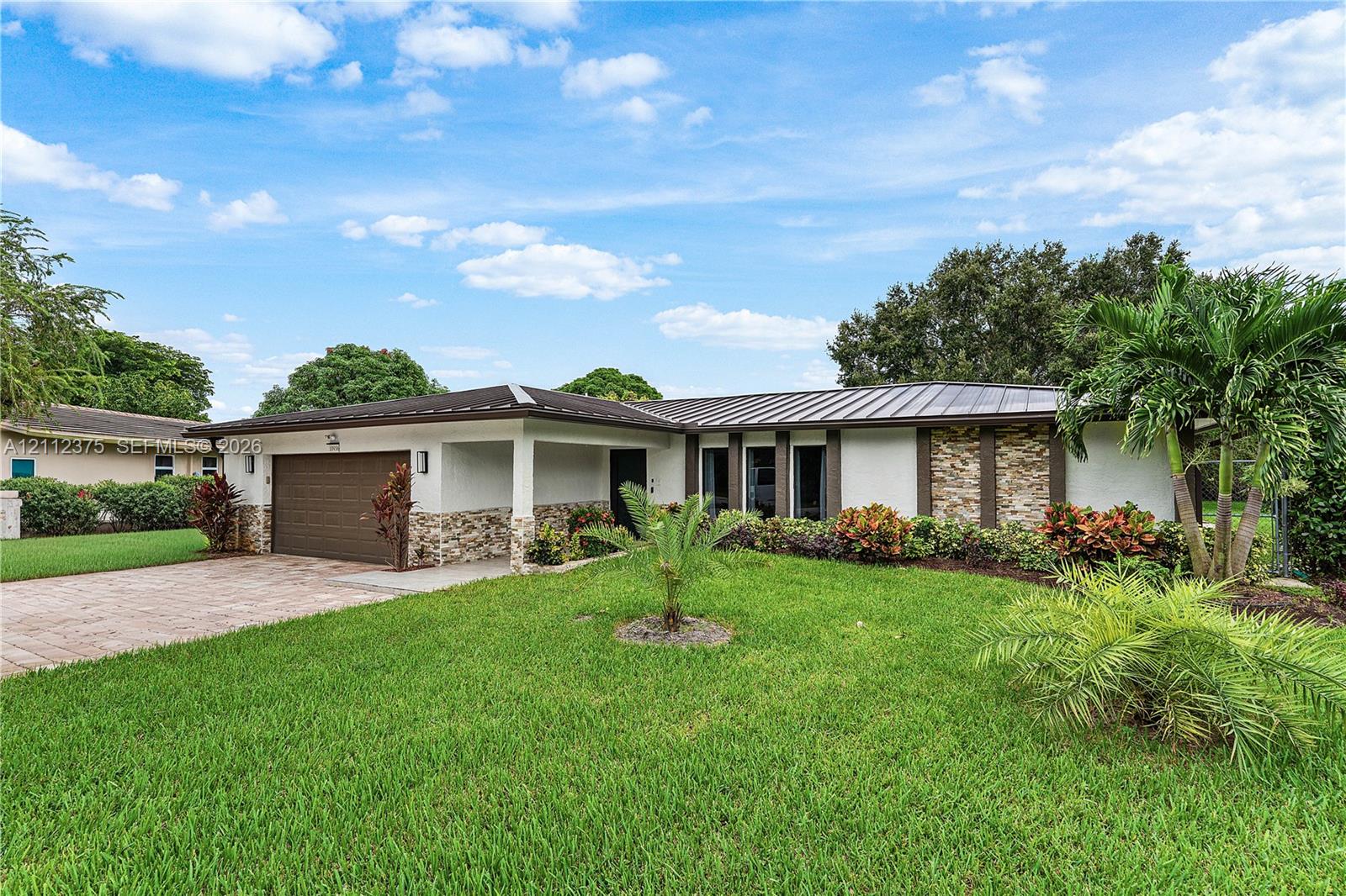 Single-story exterior featuring a metal roof, stone-veneer accents, an attached two-car garage, and a brick-paver driveway