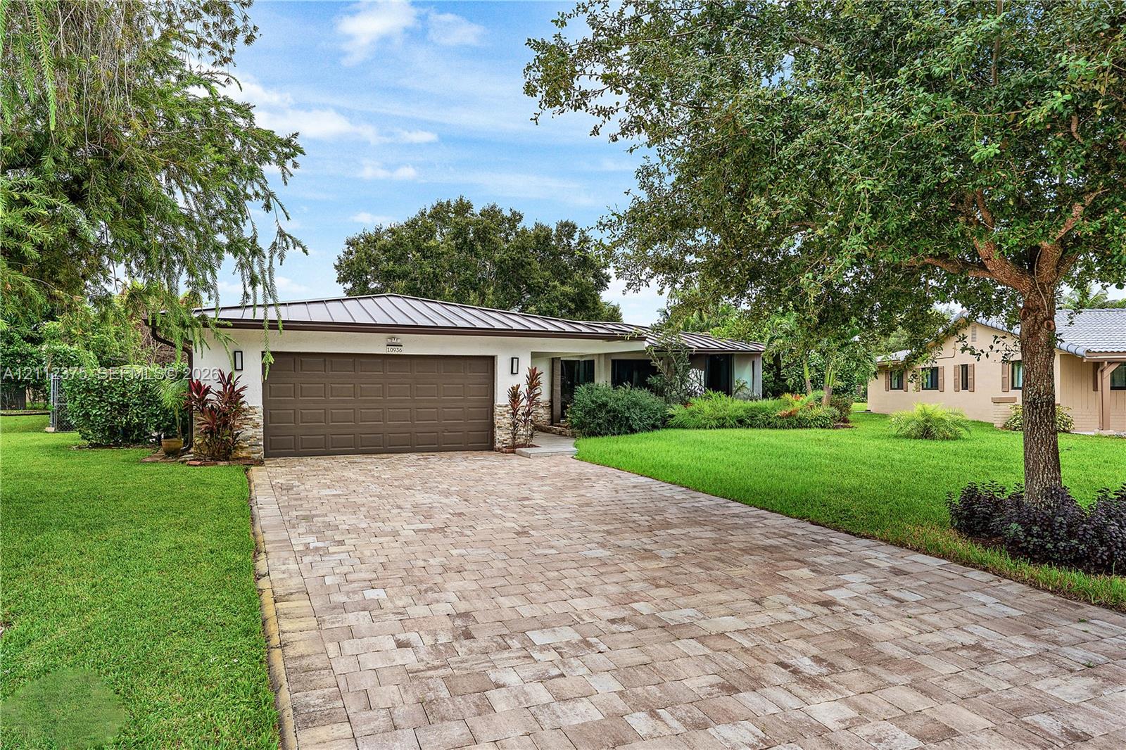 Paver driveway leading to a residence featuring a metal roof, two-car garage, and stone-accented exterior