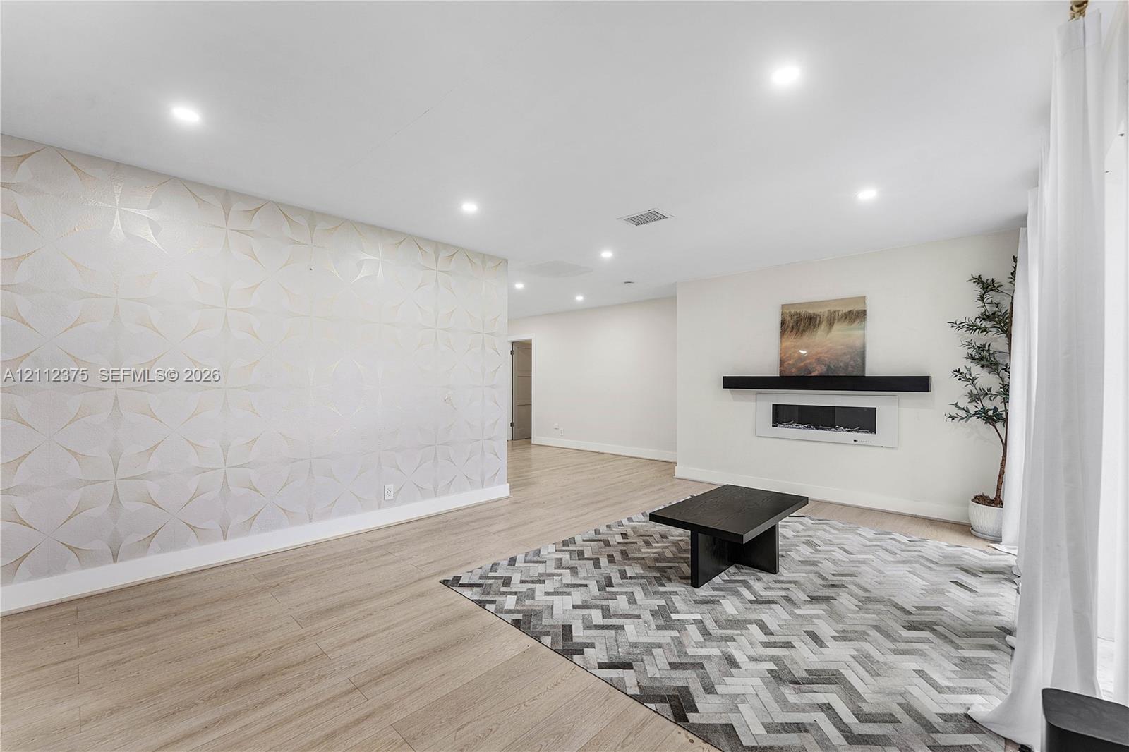 Living area featuring light-toned wood-finish flooring, recessed lighting, a patterned textured accent wall, and a linear wall-mounted electric fireplace with a floating mantel