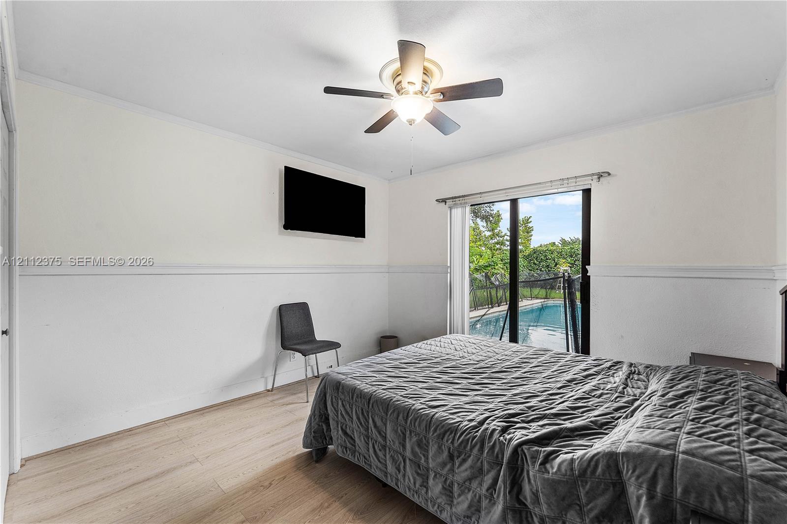 Neutral-toned interior featuring wood-finish flooring, chair rail molding, ceiling fan with integrated lighting, and glass sliding doors