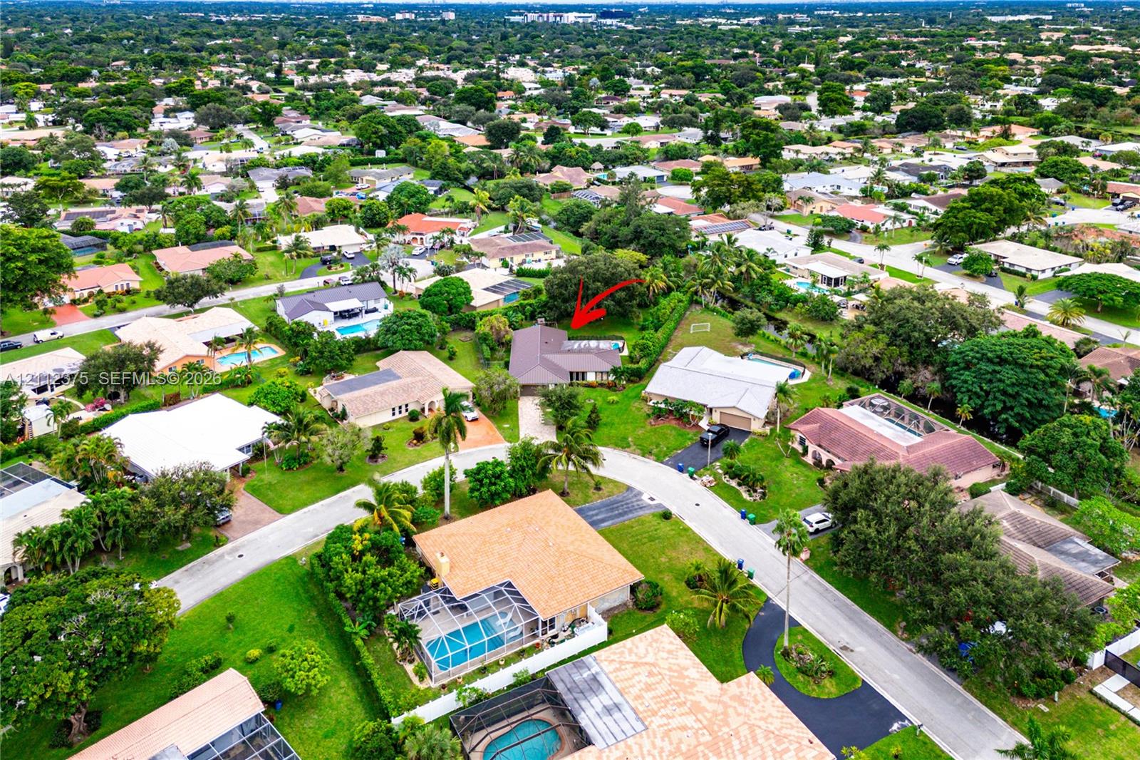 Aerial perspective of a single-story residence featuring a shingled roof, a paved driveway, and a rear swimming pool