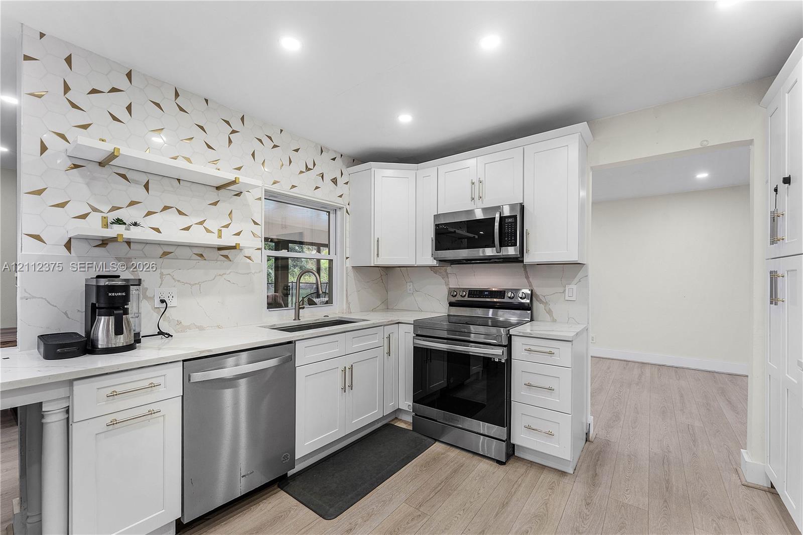 Kitchen featuring white shaker-style cabinetry, quartz countertops, geometric pattern backsplash, wood-finish flooring, and stainless steel appliances