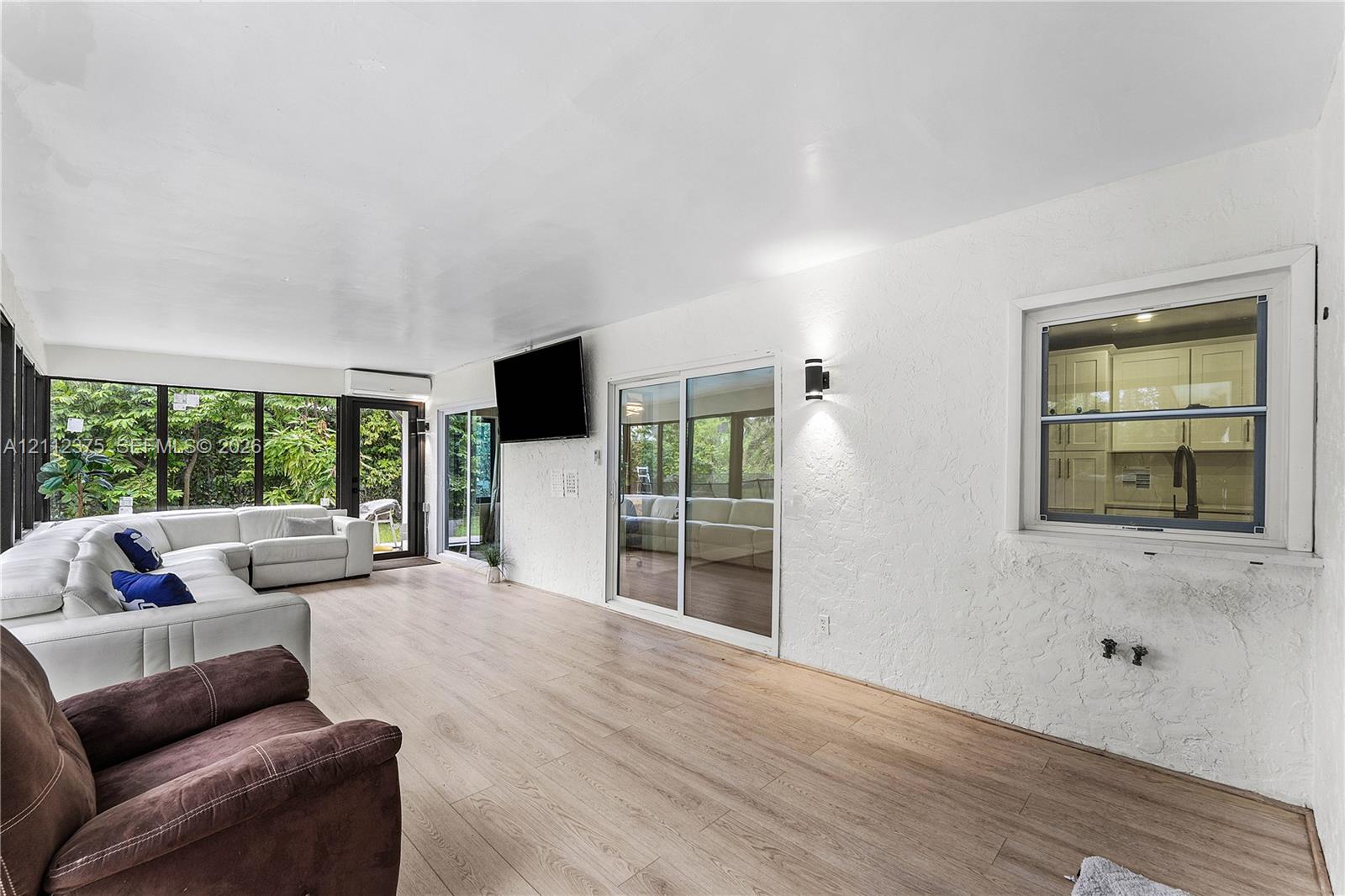 Sunroom featuring wood-finish flooring, textured walls, sliding glass doors, wall-mounted light fixtures, and windows with integrated screens