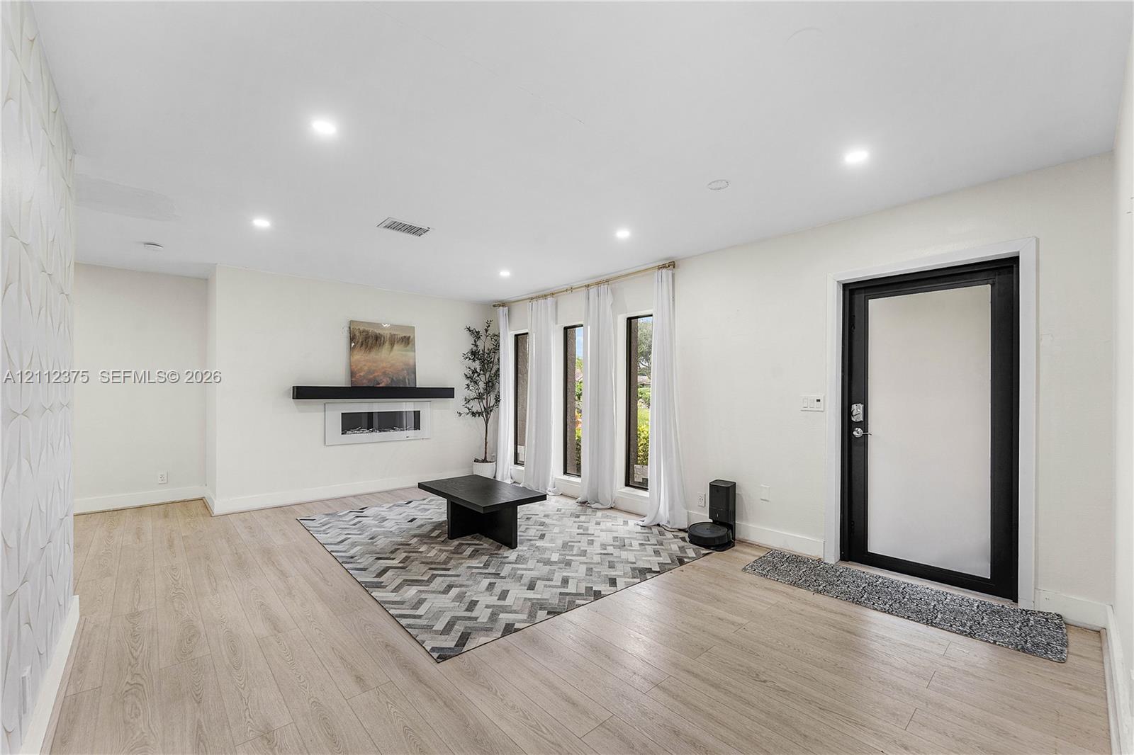Open-concept room featuring wood-finish flooring, recessed lighting, a textured accent wall, and a linear wall-mounted fireplace with a mantel