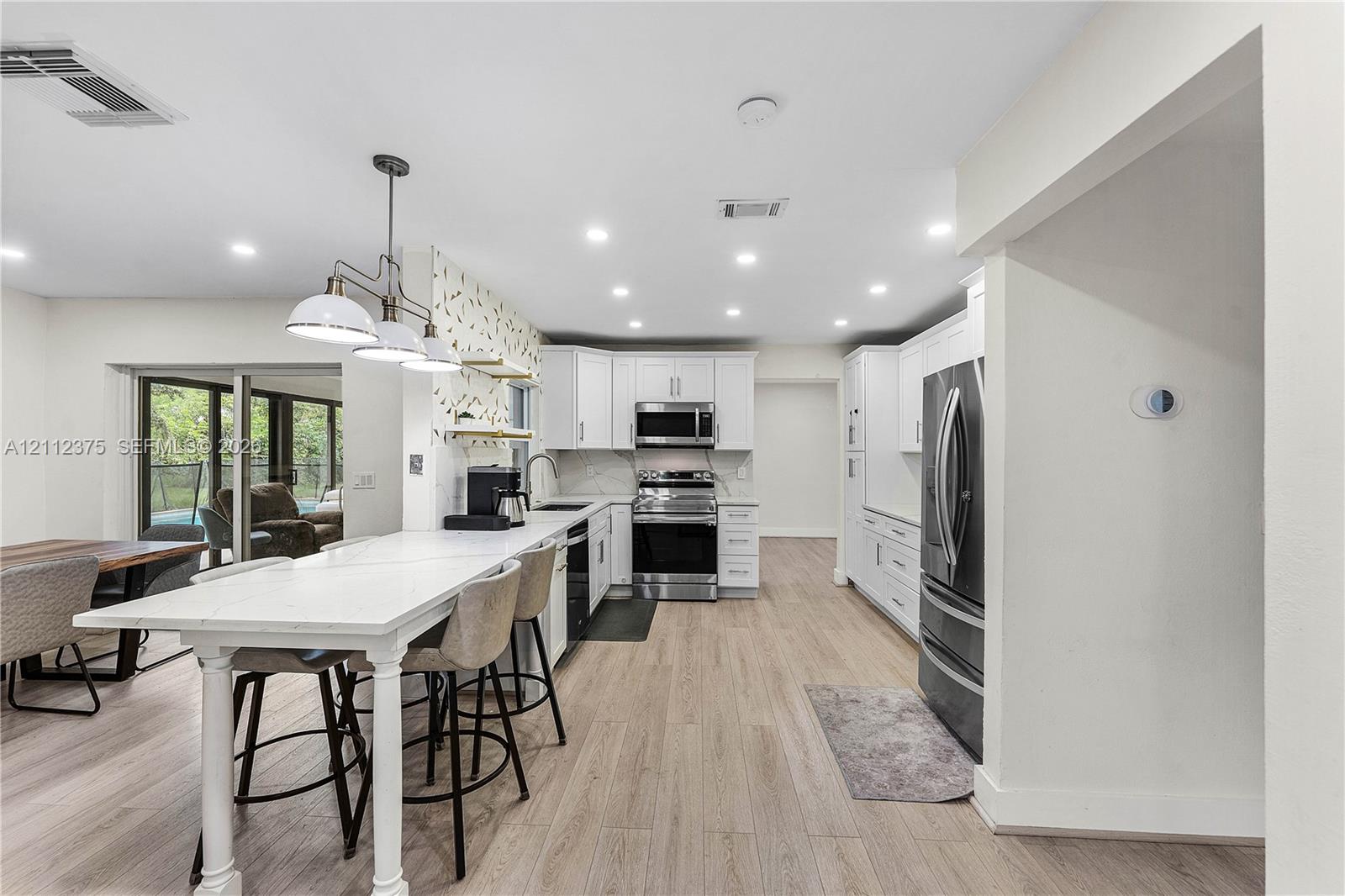Kitchen featuring wood-finish flooring, white cabinetry, integrated stainless steel appliances, and an extended peninsula with a stone-surface countertop