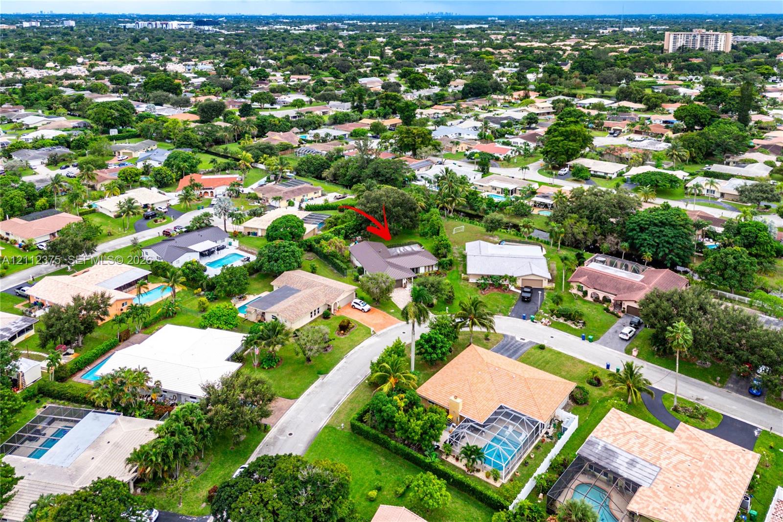 Aerial perspective of a residential property featuring a pitched roof, attached garage, paved driveway, and mature landscaping within a suburban setting