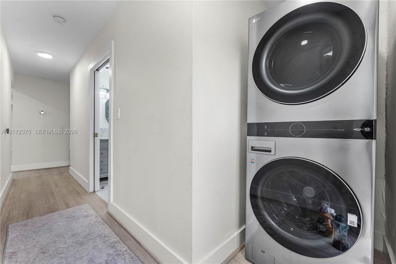 Laundry closet featuring a stackable stainless-steel washer and dryer unit with wood-finish flooring