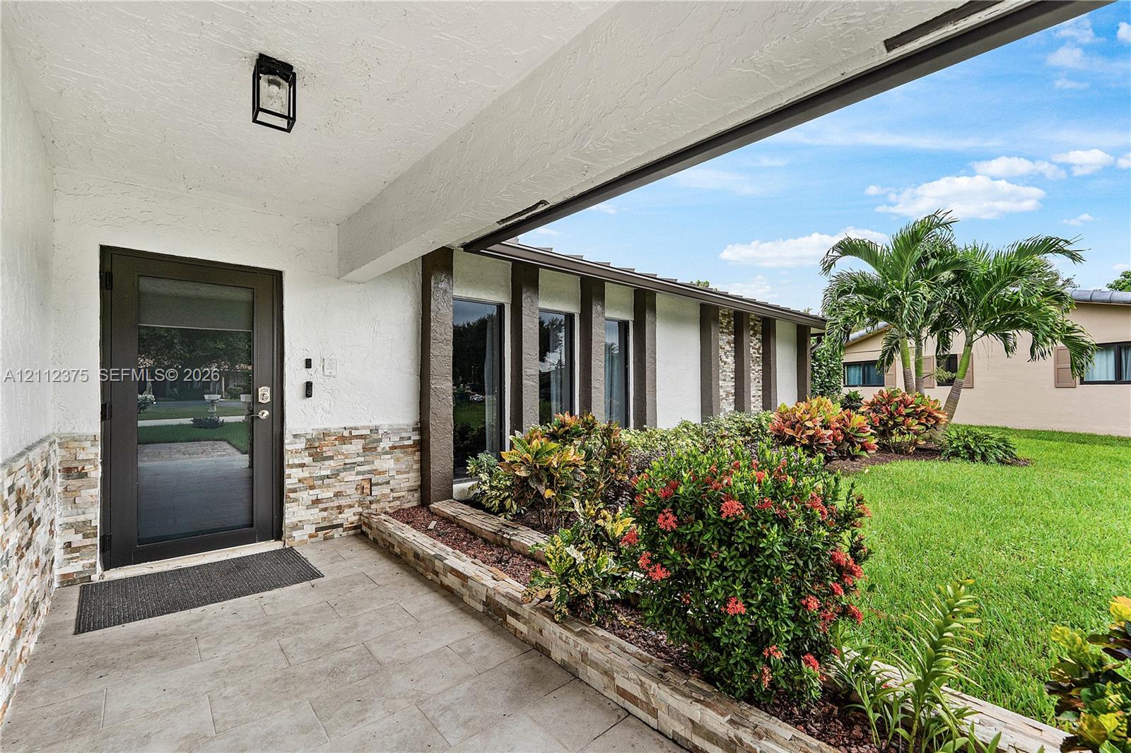Covered entryway featuring stacked stone accents, tile flooring, a glass-panel entry door, and exterior wall-mounted lighting