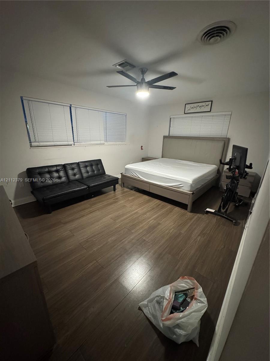 Room featuring wood-finish flooring, a multi-blade ceiling fan with integrated lighting, and horizontal slatted window blinds