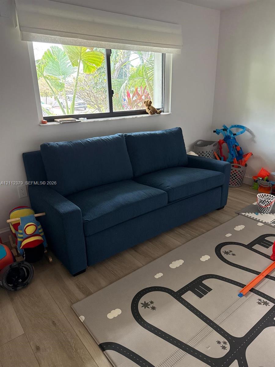 Room featuring wood-finish flooring, a single-hung window with a fabric roller shade, and neutral wall paint