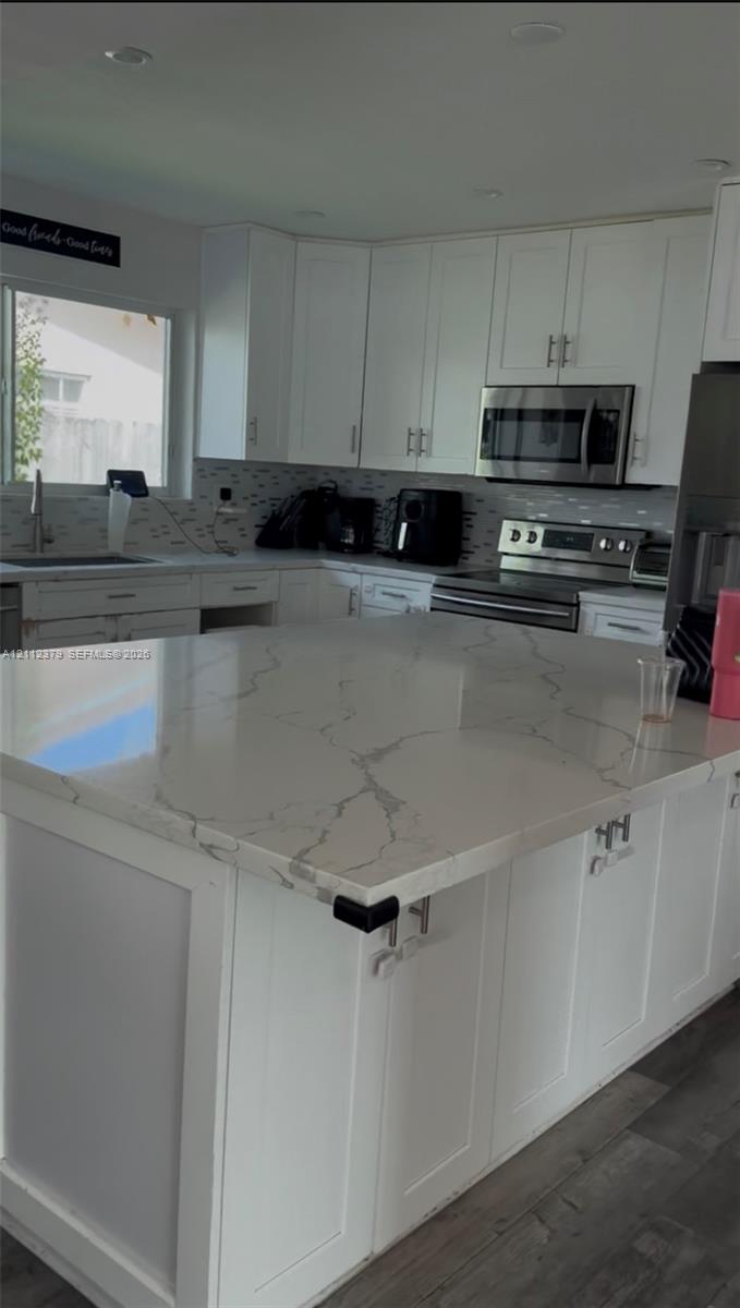 Kitchen featuring a large island with a patterned stone-surface countertop, white shaker-style cabinetry, stainless steel appliances, and wood-finish flooring