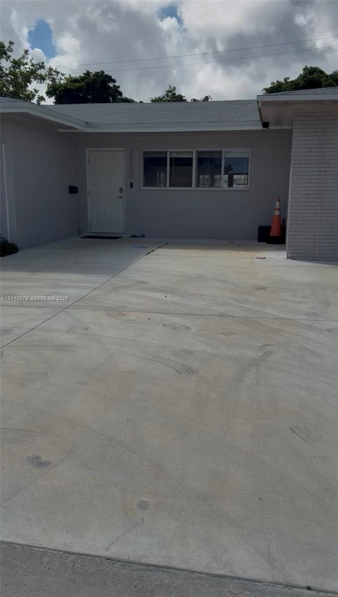 Exterior entrance featuring a concrete driveway, painted stucco facade, brick siding accents, and a panelled entry door Exterior entrance featuring a concrete driveway, painted stucco facade, brick siding accents, and a panelled entry door
