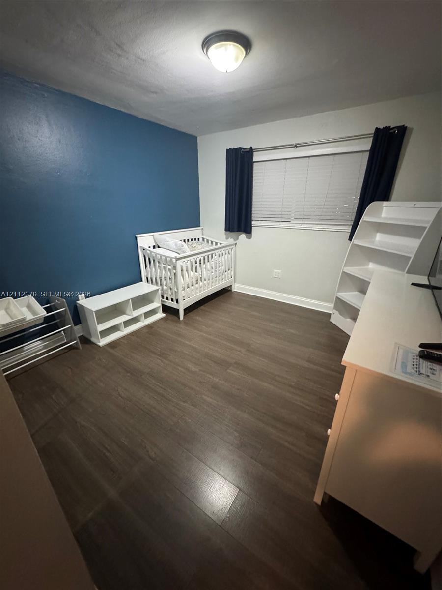 Room featuring wood-finish flooring, a bold accent wall, and a horizontal window with adjustable blinds