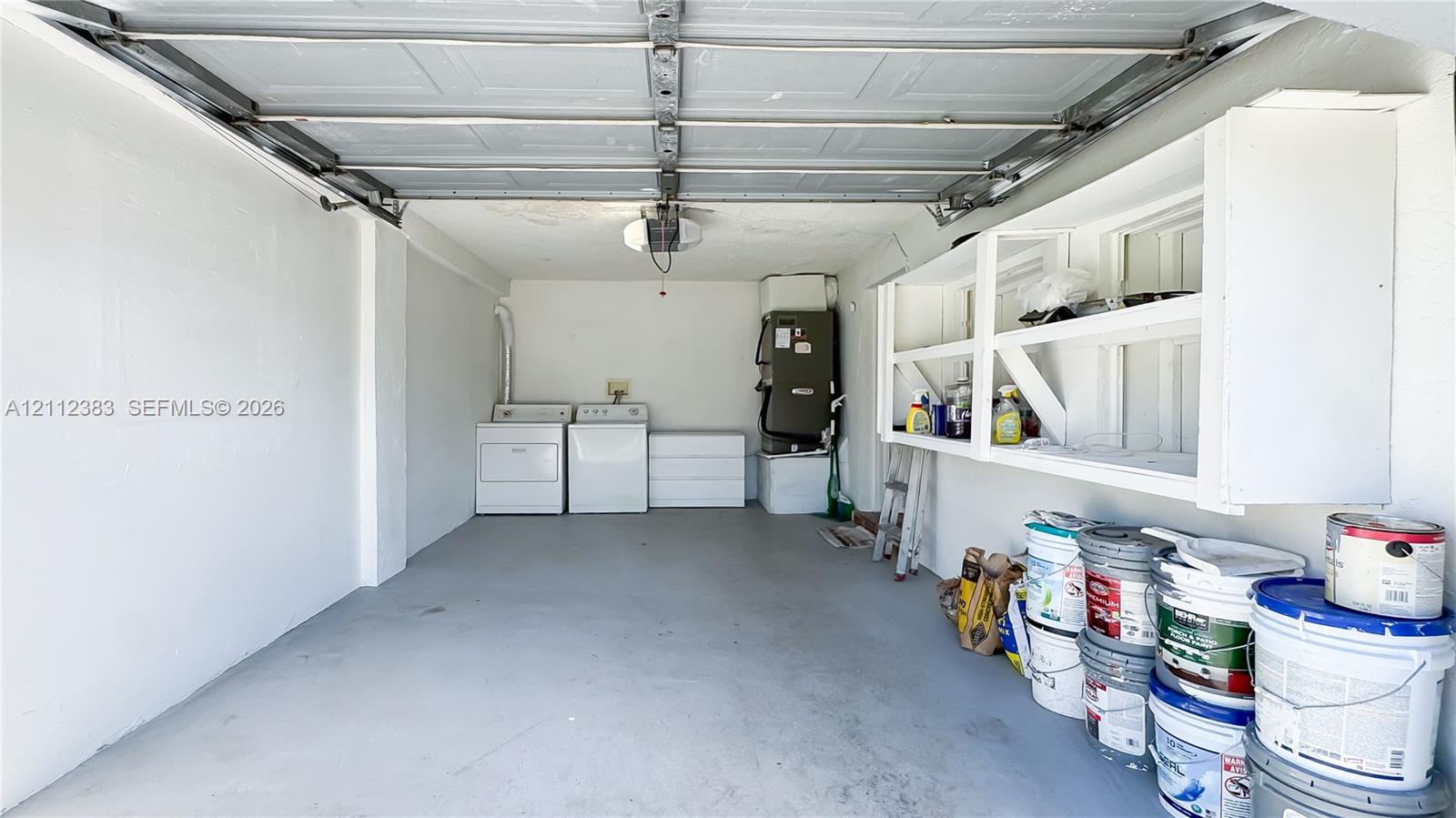 Enclosed garage space featuring overhead sectional door, dedicated laundry area with side-by-side connections, and built-in wall-mounted shelving units