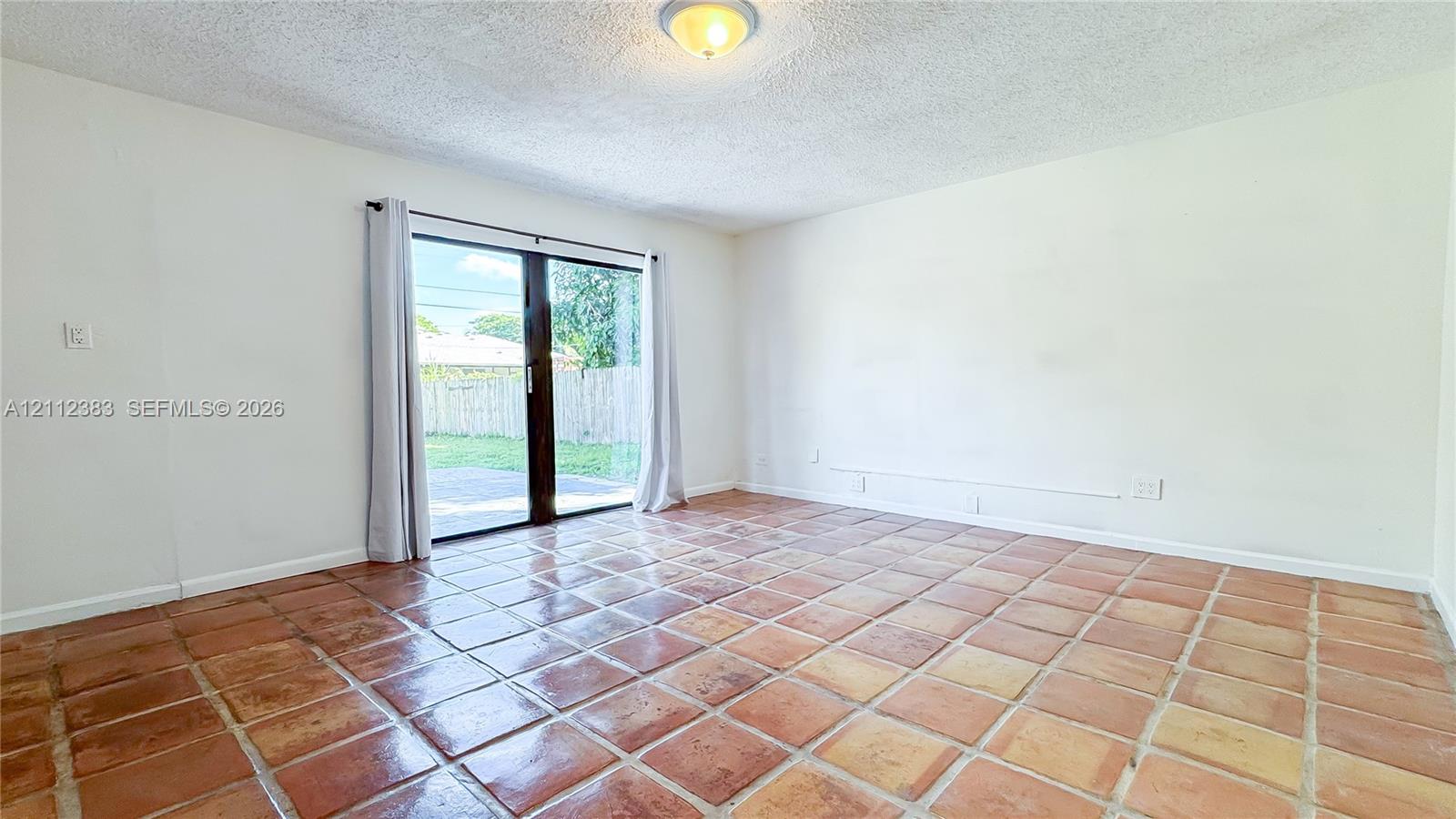 Interior room featuring terracotta tile flooring, sliding glass door, flush-mount lighting, and neutral wall paint