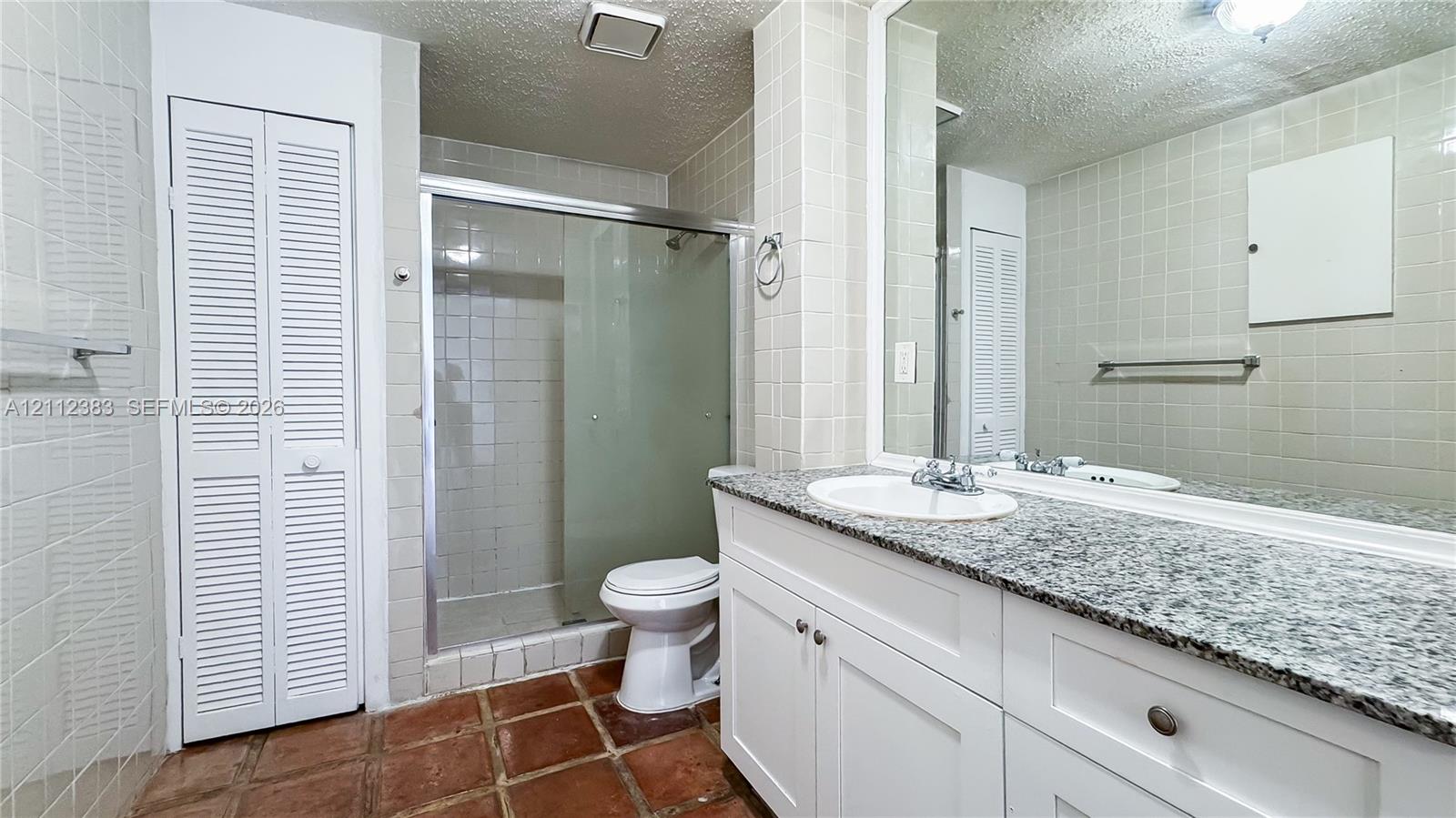 Bathroom featuring a vanity with a stone countertop, an integrated sink, a large wall-mounted mirror, a glass-enclosed shower, and tile flooring