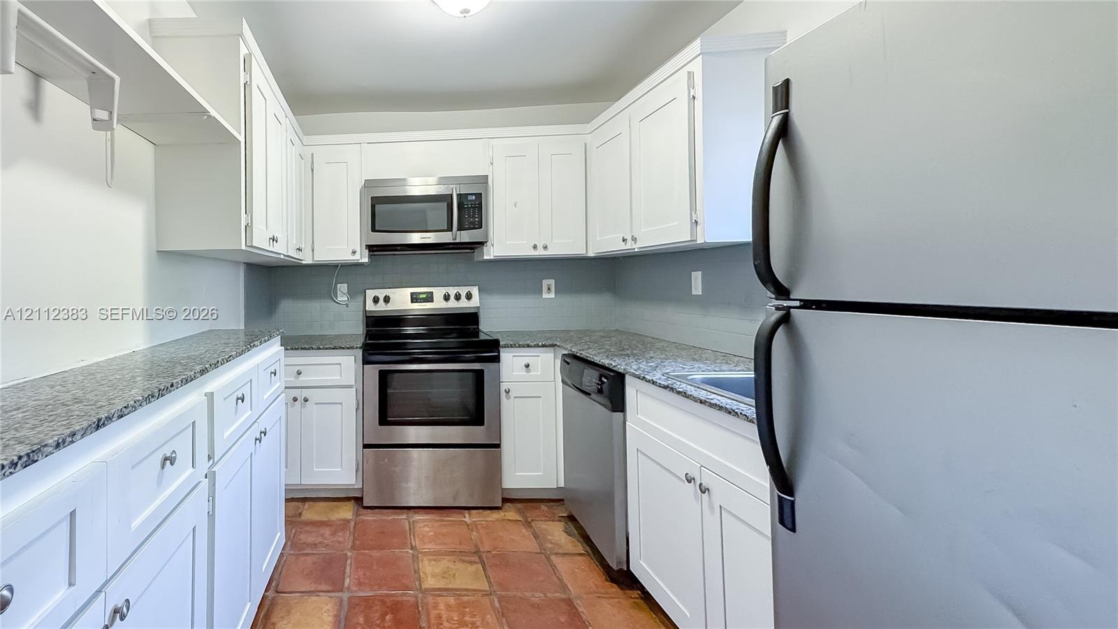 Kitchen featuring white cabinetry, stone-finish countertops, stainless steel appliances, and terra-cotta tile flooring