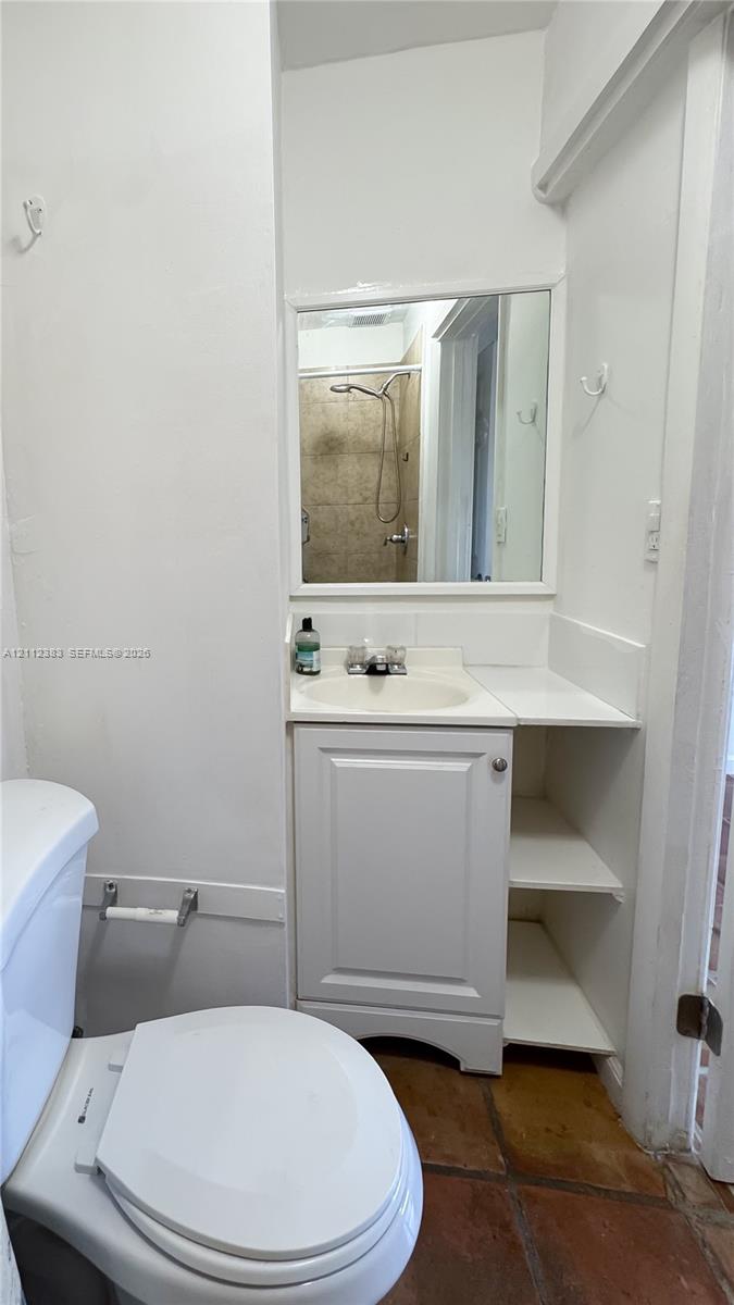 Bathroom featuring a vanity with integrated shelving, inset sink, framed wall mirror, and terra-cotta tile flooring