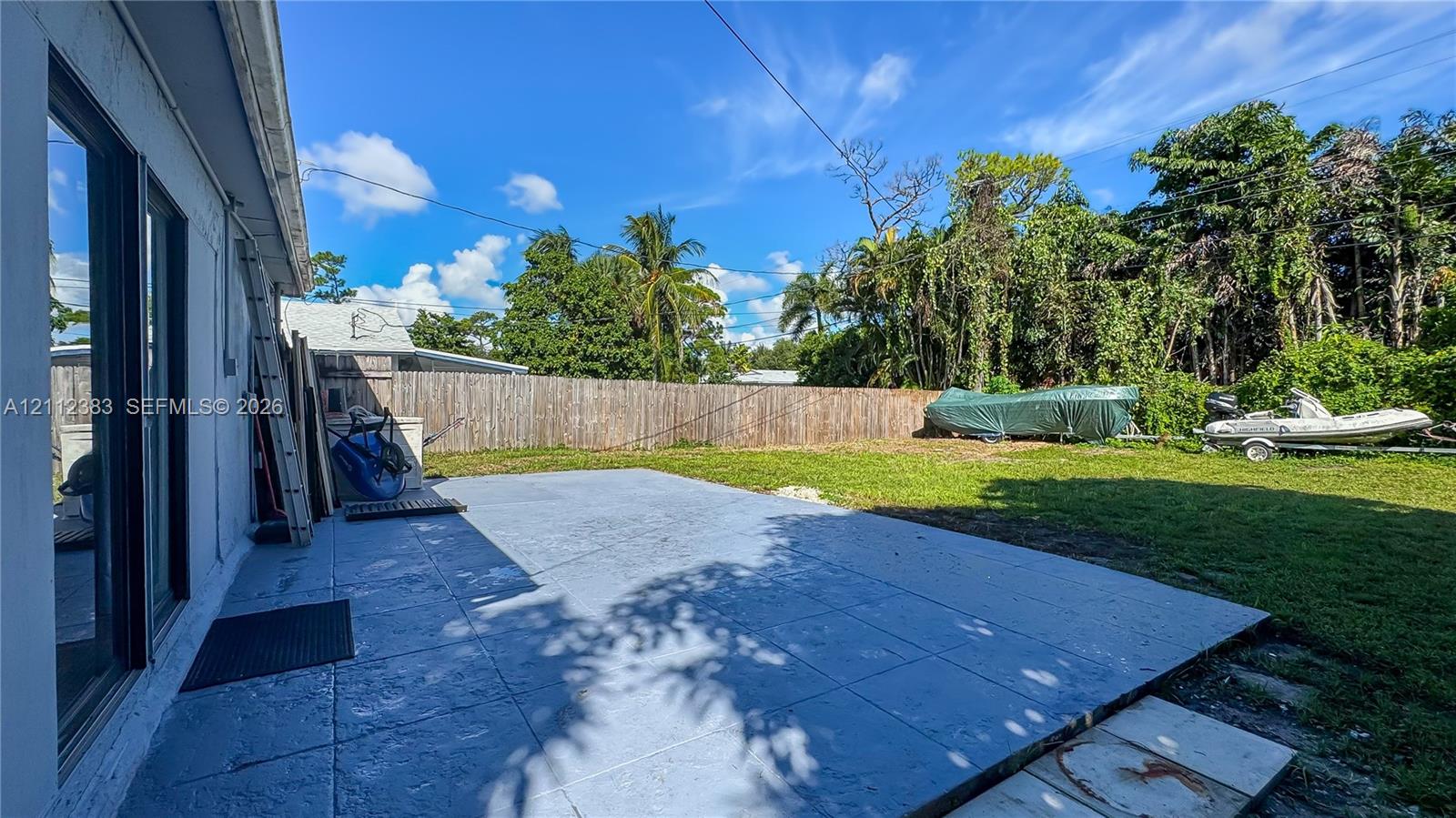 Concrete patio slab featuring a textured surface, enclosed by a wood perimeter fence, and accompanied by a grass lawn