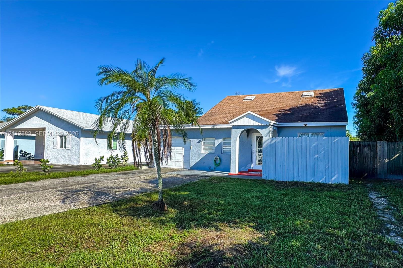Single-story residence featuring a blue stucco exterior, gabled roof with skylights, an arched covered entryway, and a private wooden fence