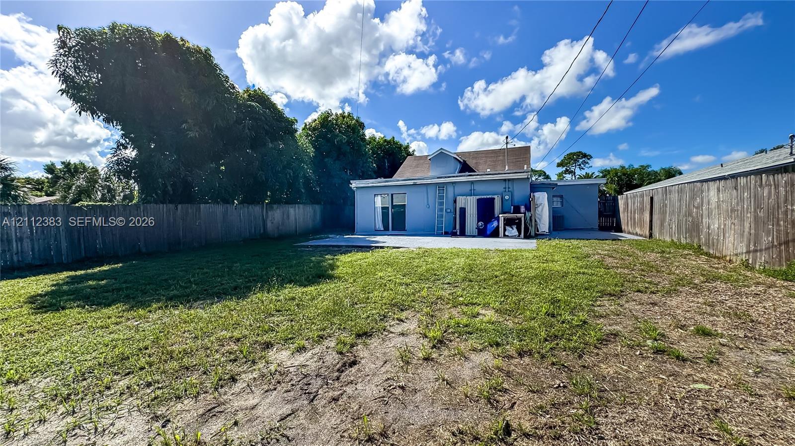 Fenced backyard featuring a concrete patio, grassy lawn, and perimeter wood fencing