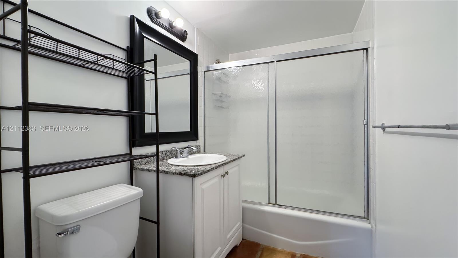Bathroom featuring a white vanity with a stone-finish countertop, undermount sink, framed wall mirror, and a tub-shower combination with sliding glass doors