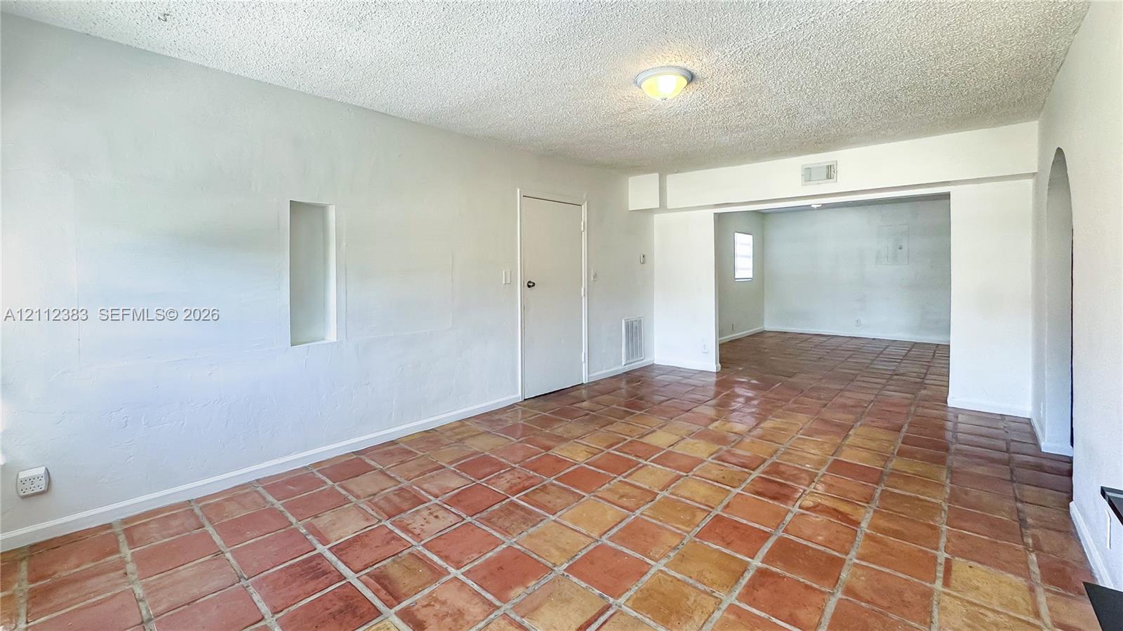 Interior featuring terra-cotta tile flooring, arched wall opening, recessed wall niche, and flush-mount ceiling lighting