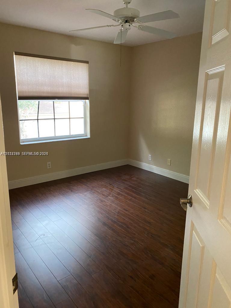 Interior room featuring wood-finish flooring, multi-pane window with custom roller shade, and ceiling-mounted fan with light fixture