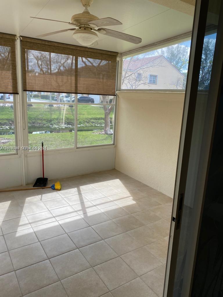 Enclosed patio featuring light-toned tile flooring, large windows, a ceiling fan, and privacy shades