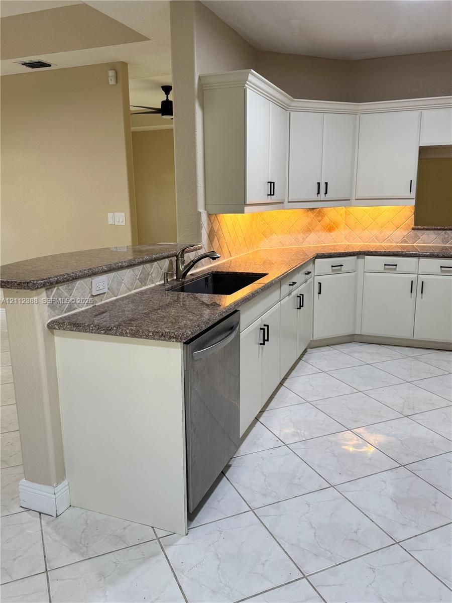 Kitchen featuring white cabinetry with matte black hardware, stone-finish countertops, tile backsplash, stainless steel dishwasher, and tile flooring