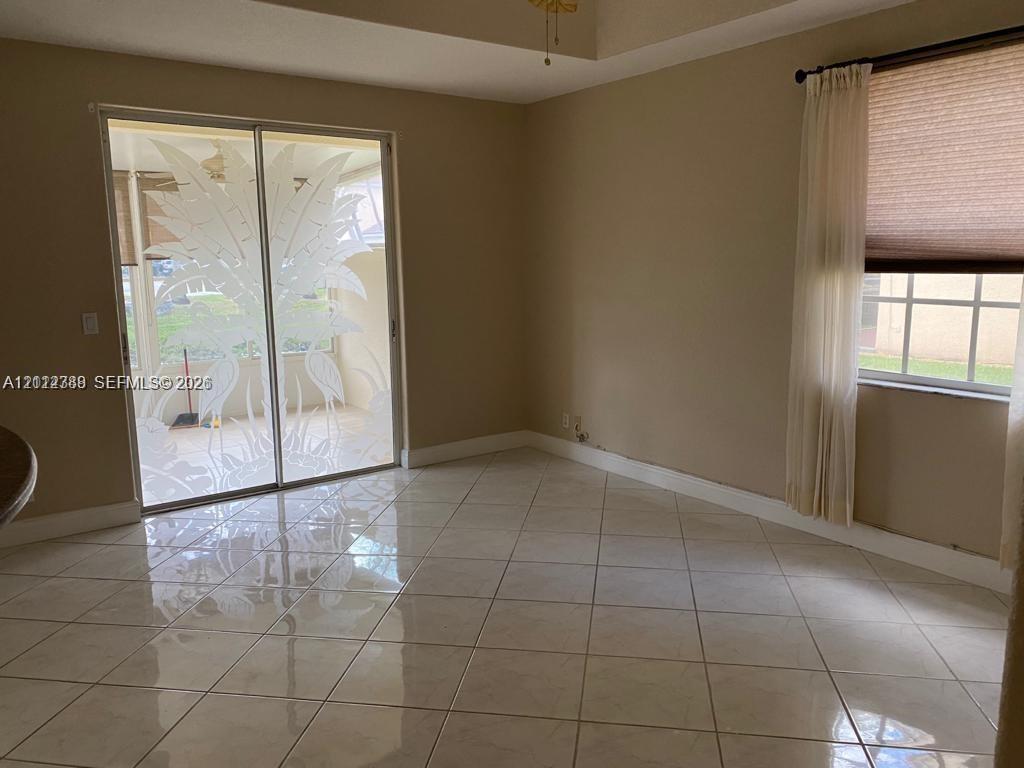 Interior space featuring polished ceramic tile flooring, a tray ceiling, and sliding glass doors with decorative etched glass