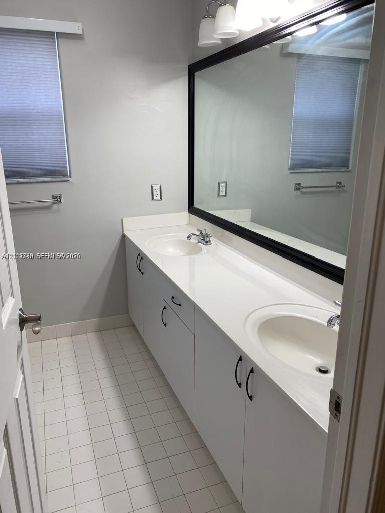 Double vanity with integrated sinks, white countertops, white cabinetry with matte black hardware, large-format mirror with black frame, and tiled flooring