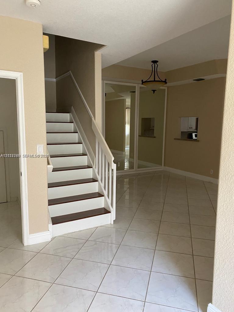 Tiled flooring, staircase with a wooden handrail, mirrored wall panels, and a multi-arm pendant light fixture