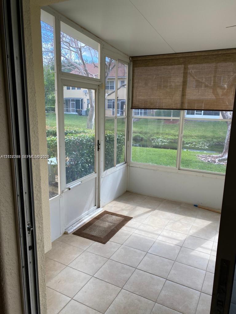 Screened-in enclosure featuring neutral ceramic tile flooring, full-height window panels, and a glass-paneled entry door