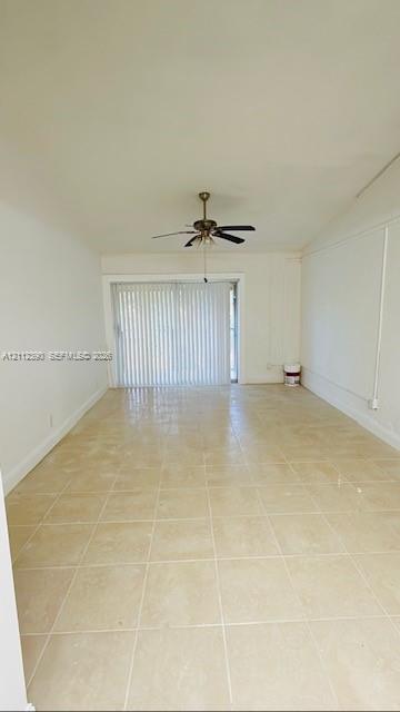 Interior space featuring large-format neutral floor tile, a vaulted ceiling, and a central ceiling fan with integrated lighting Interior space featuring large-format neutral floor tile, a vaulted ceiling, and a central ceiling fan with integrated lighting