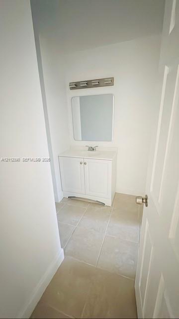 White vanity cabinet with a solid surface countertop, rectangular mirror, multi-bulb vanity light, and neutral tile flooring White vanity cabinet with a solid surface countertop, rectangular mirror, multi-bulb vanity light, and neutral tile flooring