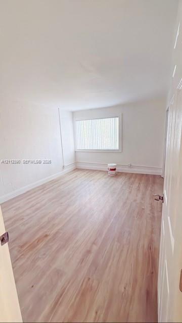 Interior space featuring wood-finish flooring, white walls, and a large window with vertical blinds Interior space featuring wood-finish flooring, white walls, and a large window with vertical blinds