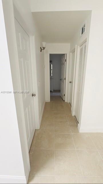 Hallway featuring neutral large-format tile flooring, multi-panel doors, white louvered closet doors, and wall-mounted sconce lighting