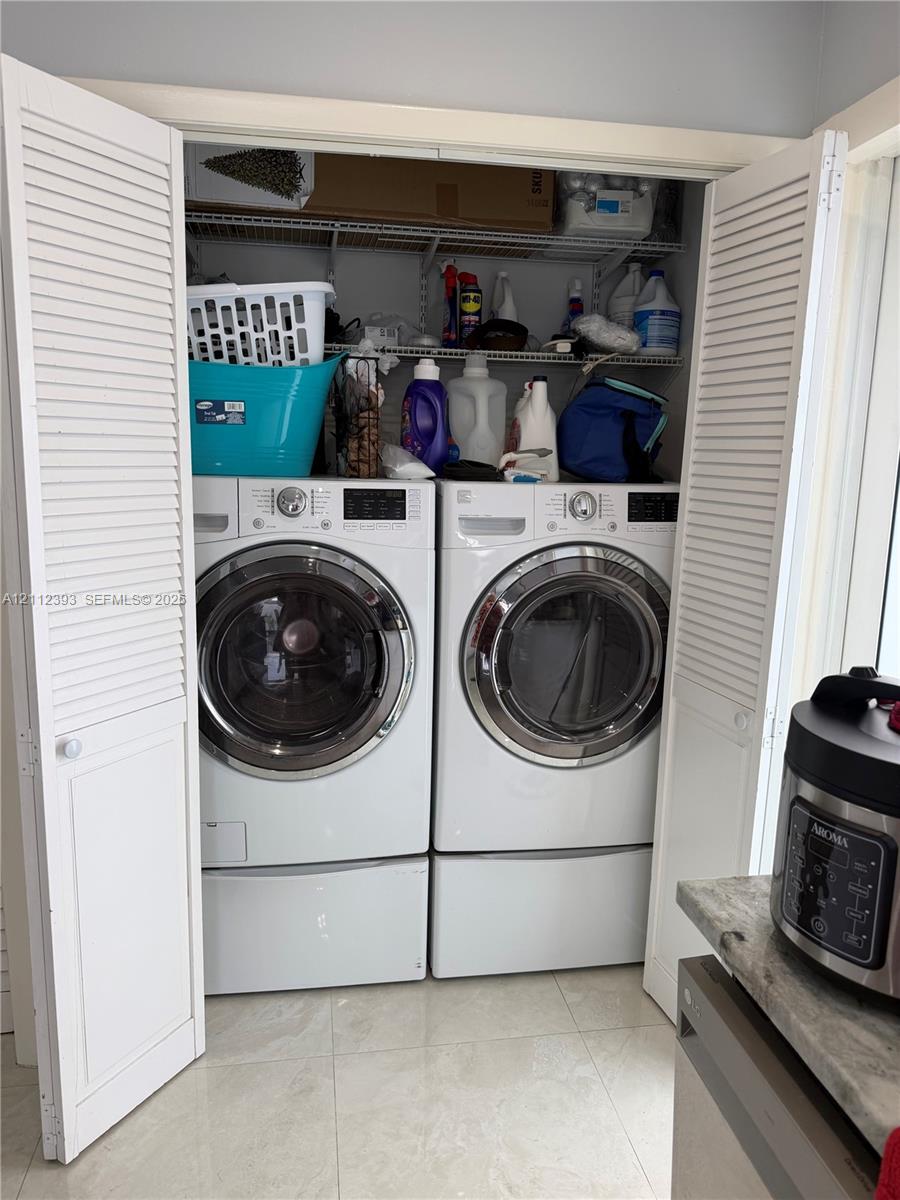 Laundry closet featuring dual white louvered bi-fold doors, stacked wire shelving, and neutral-toned tile flooring