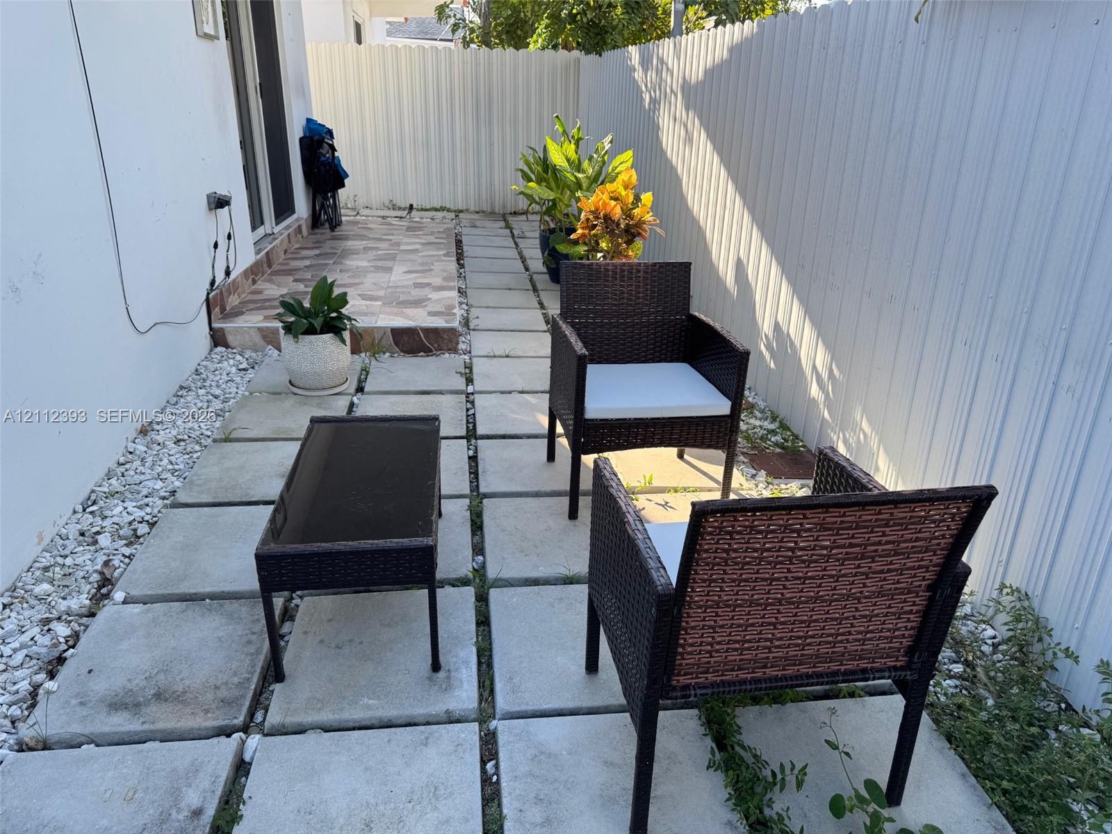 Outdoor space featuring large-format concrete pavers, patterned tile patio area, decorative white stone ground cover, and full-height privacy fencing