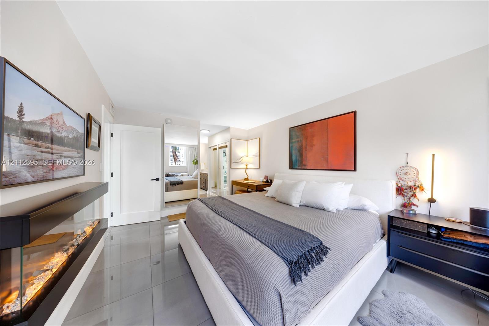 Large-format polished tile flooring, wall-mounted electric fireplace, and mirrored closet doors