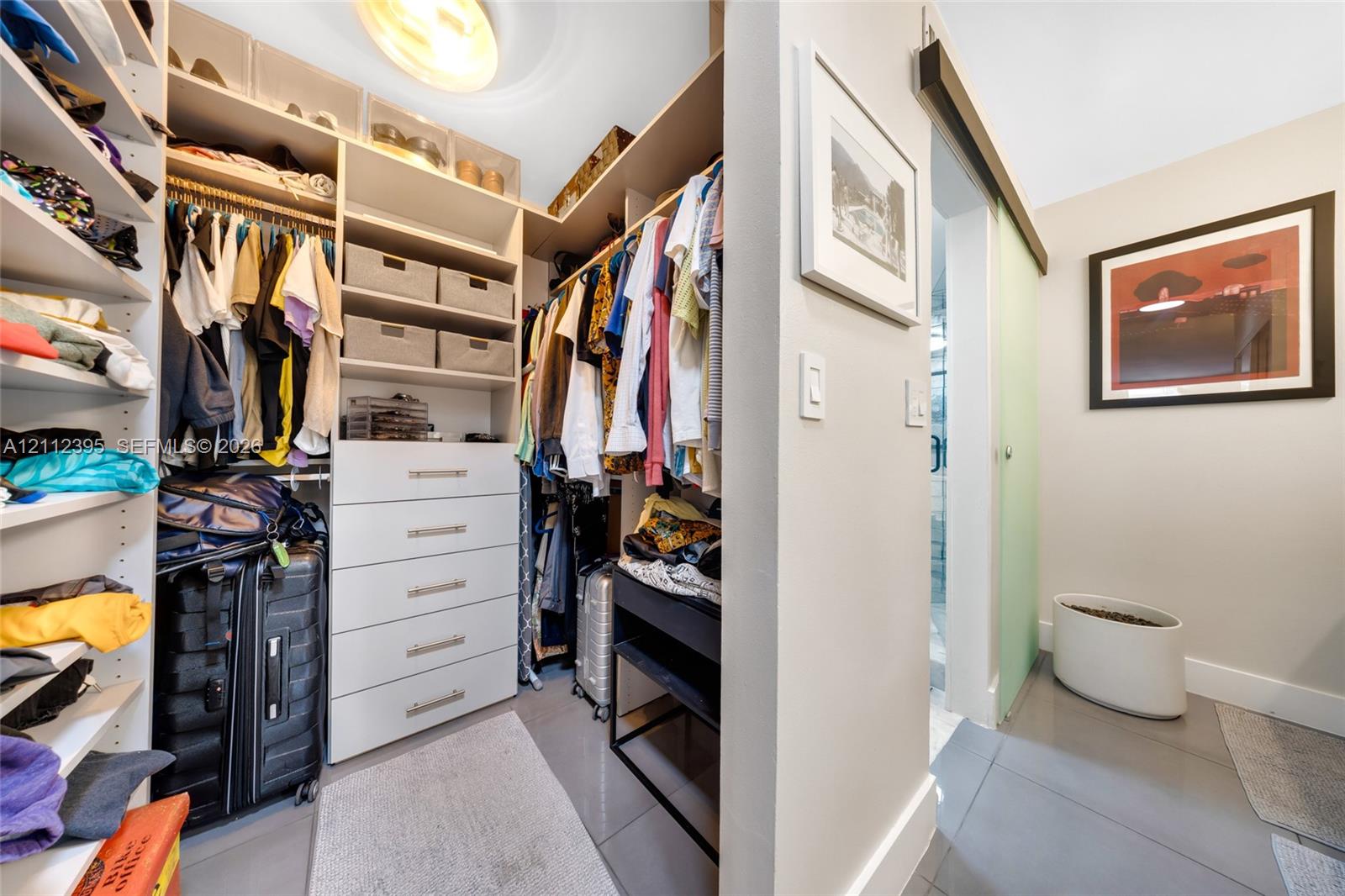Custom walk-in closet featuring multi-level hanging rods, integrated storage shelving, a five-drawer built-in cabinet, and a sliding door entrance