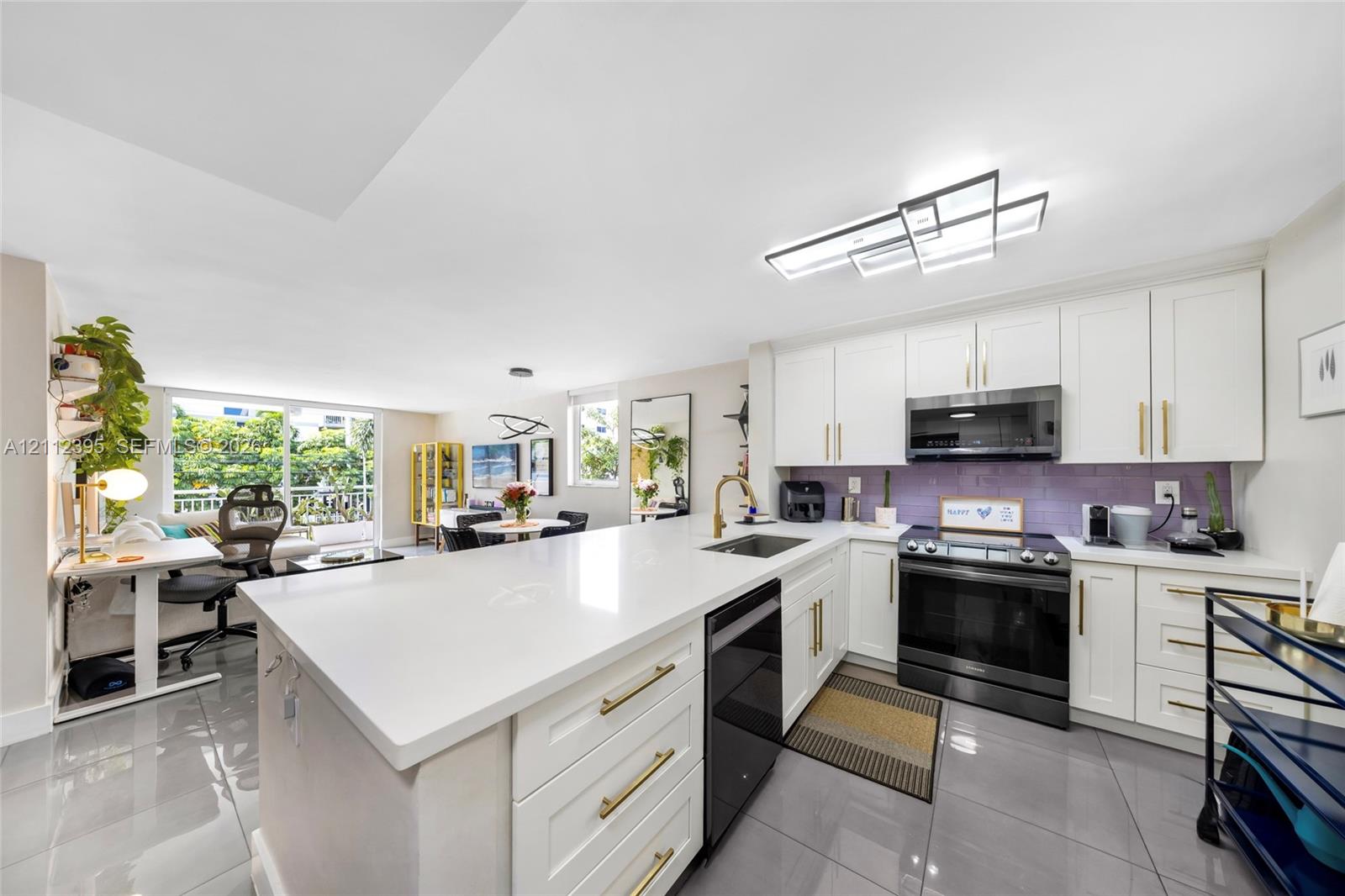 Kitchen featuring a central island with a quartz countertop, white shaker-style cabinetry with gold-tone pulls, a purple tile backsplash, large-format tile flooring, and contemporary geometric overhead lighting
