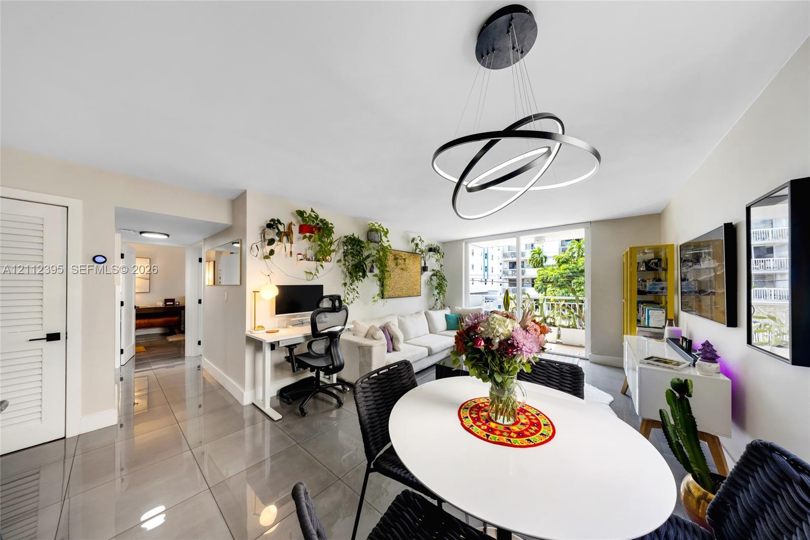 Living area featuring polished large-format floor tiles, contemporary multi-ring circular pendant lighting, and glass sliding doors providing external access